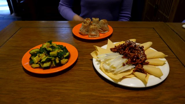 Beijing style meals served at restaurant, Jing Jiang Rou Si and smashed cucumbers salad, woman touch and turn plate with dumplings on background