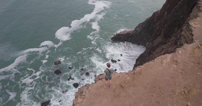 This is a smooth aerial shot showing a person standing on the edge of a cliff near Paracas in Peru.
