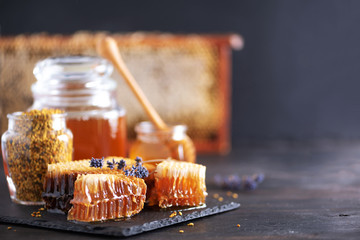 Bee pollen granules, honey jar with wooden dropper, honeycomb on dark backdrop. Copy space. Autumn harvest concept