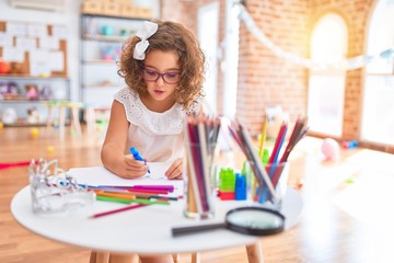 Beautiful toddler wearing glasses sitting drawing using paper and marker pen at kindergarten