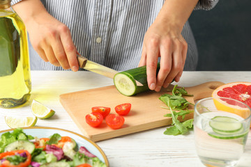 Young woman slices cucumber for salad on wooden background