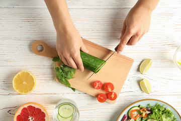 Young woman slices cucumber for salad on wooden background, top view