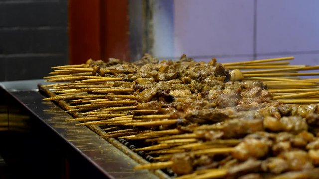 Traditional grilled meat on sticks cooked at street of Beijing, close up shot of many wooden sticks of Shaokao lying on grill, smoke rise up from hot meal