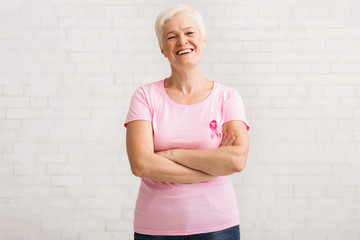 Senior Woman In Pink Breast Cancer T-Shirt Standing Over White Wall