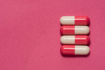 Red and white capsules pills set in a line, closeup. Isolated on pink background.