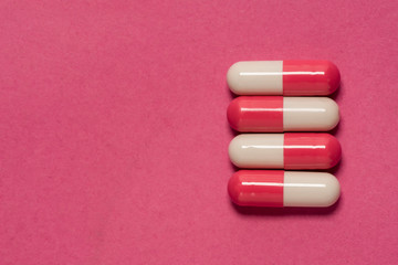 Fototapeta na wymiar Red and white capsules pills set in a line, closeup. Isolated on pink background.