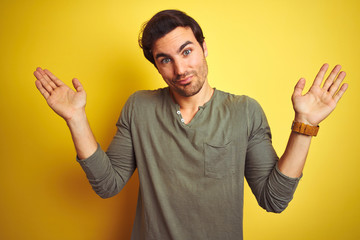 Young handsome man wearing casual t-shirt standing over isolated yellow background clueless and...