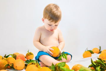 Fototapeta na wymiar Cute blond baby playing with oranges on a light background.
