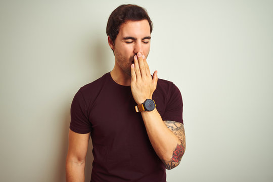 Young handsome man with tattoo wearing purple casual t-shirt over isolated white background bored yawning tired covering mouth with hand. Restless and sleepiness.