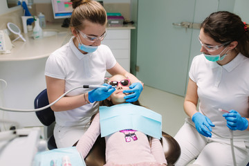 Little girl in 3D glasses sitting on destal chair at the office and have yearly checkup. Dentist with assistant