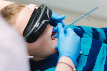 Close up of little boy sitting in dentist in vr glasses and wireless headphones while dentist make x-ray of teeth