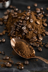 Grained coffee powder on rose gold spoon and coffee beans over black marble surface.