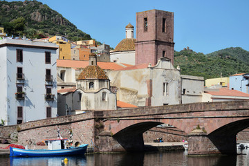 Fototapeta na wymiar Traditional fishing boat moored near a bridge on the Temo river in the city of Bosa. The ancient city palaces and a church in the background
