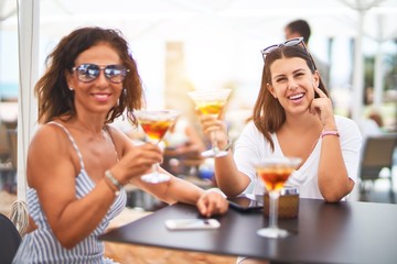 Beautiful mother and daugther sitting at terrace of restaurtant drinking cocktail speaking and smiling