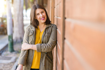 Beautiful young woman smiling confident and cheerful leaning on wooden wall, walking on the street of the city on a sunny day