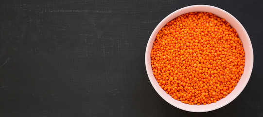 Red lentils in a pink bowl on a black surface, top view. Flat lay, overhead, from above. Copy space.