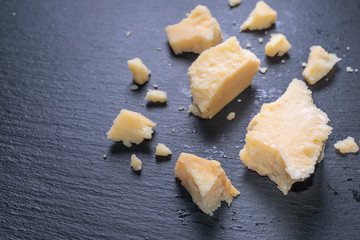 close up of tasty fresh pieces cheese parmigiano on black slate background