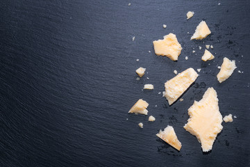 top view of tasty fresh pieces cheese parmigiano on black slate background, copy space