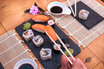 Human hand with chopsticks and a Nigiri sushi. Wooden table with sushi food