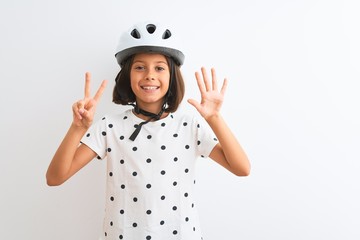 Beautiful child girl wearing security bike helmet standing over isolated white background showing and pointing up with fingers number seven while smiling confident and happy.