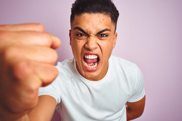 Young brazilian man wearing t-shirt standing over isolated pink background annoyed and frustrated shouting with anger, crazy and yelling with raised hand, anger concept