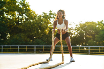 Photo of beautiful focused woman doing workout with battle ropes