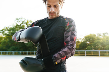 Photo of unshaven thinking man putting boxing gloves at playground