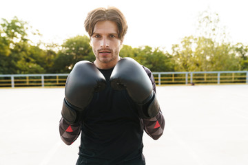 Fototapeta na wymiar Photo of handsome confident man doing workout in boxing gloves