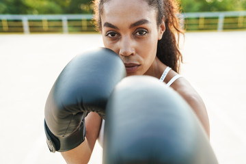 Photo of strong woman in boxing gloves hitting at camera
