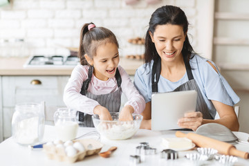 Mother and daughter using digital tablet in kitchen, looking recipe