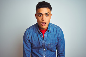 Young brazilian man wearing denim shirt standing over isolated white background afraid and shocked with surprise expression, fear and excited face.