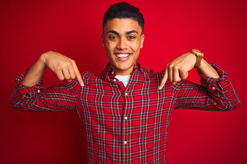 Young brazilian man wearing shirt standing over isolated red background looking confident with...