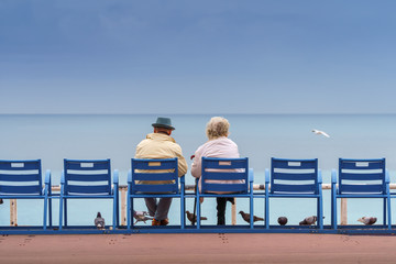 Old couple sitting on the bank of the sea. Happy and long life together.
