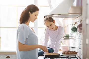 Fototapeta premium Happy young mother and daughter cooking together in kitchen
