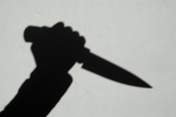 Knife in a hand shadow on a gray wall