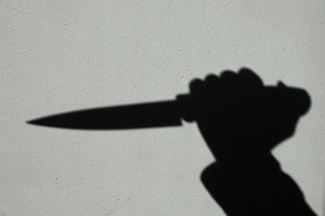 Knife in a hand shadow on a gray wall