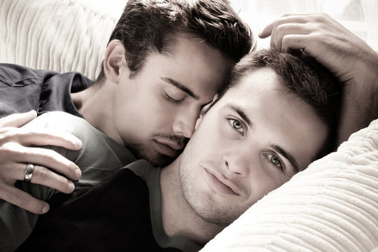 Smiling handsome gay man looks at camera as his partner or husband kisses his cheek