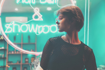 Hipster teen tomboy girl pretty face short hairstyle wear stylish glasses on neon sign background,...