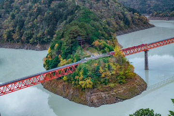 Fototapeta premium Okuoikojo Station, a landmark in Shizuoka Japan. A train station with two side of red rail way over the blue color water in dam. Surrounded by beatiful autumn color.