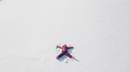 Kid on a snow making a snow angel. Aerial shot from above. She is wearing red clothes © 4Max