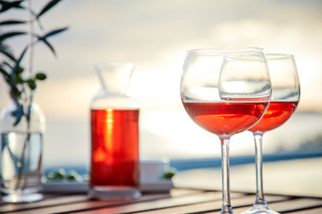two glasses of rose wine with  olives against blue water on a pier..