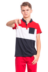 Portrait of teen boy giving thumb down gesture looking with negative expression and disapproval. Handsome caucasian young teenager doing bad signal, isolated on white background.