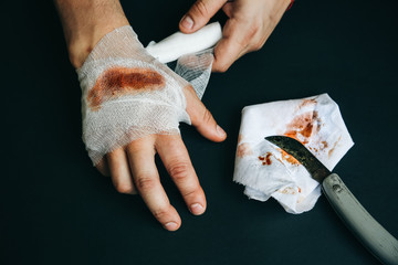 Man is putting the bandage on the wound. Bleeding injury. Deep cut with a knife.