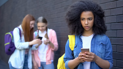 Sad african schoolgirl reading humiliating message, cyber bullying embarrassment