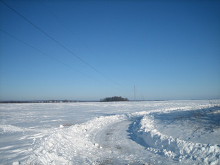 Winter road in a clean flat field on a clear frosty day. The sky is clear, blue and transparent. Snow covered the field in an endless carpet. The ruts of the road cut through the snowy surface.