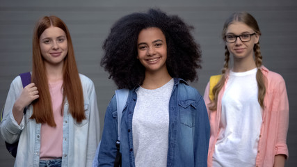 Joyful female students smiling each other grey background, international culture