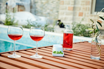 two glasses of rose wine with  olives against blue water on a pier..