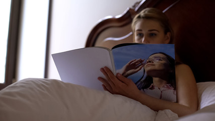 Young female reading womens magazine in bed, leisure time and relaxation