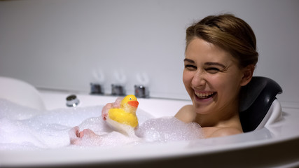 Obraz na płótnie Canvas Positive woman playing with rubber duck in bath, childish mood, having fun