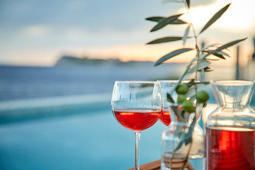 two glasses of rose wine with  olives against blue water on a pier..